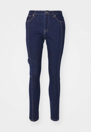Temno modri jeans z ožjim krojem, ki imajo klasičen pet-džepni dizajn in kontrastno oranžno šivanje. Brez opaznih vzorcev ali poudarkov.