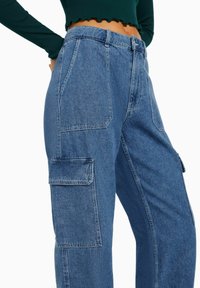 Džíny s nákladními kapsami středně modré barvy, s vysokým pasem, několika velkými kapsami a volným střihem. Texturovaná tkanina s viditelným šitím.