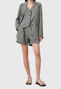 Costume gris en deux pièces comprenant un blazer ajusté et un short, fabriqué en tissu léger. Texture douce avec un design moderne et minimaliste. Sandales argentées.