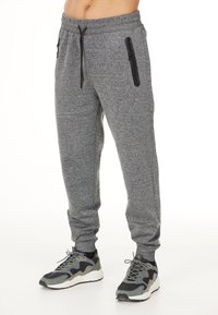Grå joggers tillverkade av mjukt, strukturerat tyg, med svarta dragkedjefickor på sidorna och ett elastiskt midjeband med dragsko.