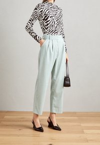 Turtleneck top s černobílým zebřím vzorem, světlemodré vysoké plisované kalhoty, černé slingback podpatky a malá černá kabelka.