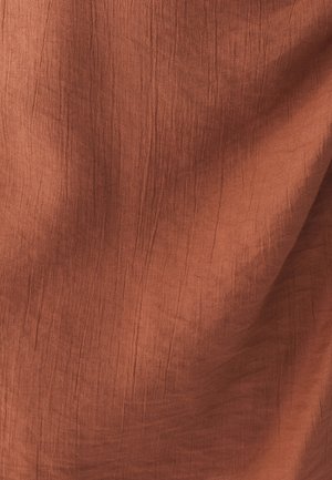 Tissu couleur rouille avec une surface texturée présentant de douces et fines rides. Le matériau semble léger et respirant.