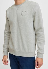 Sudadera gris hecha de un tejido suave, con un escote redondo y un pequeño detalle gráfico circular en el pecho.