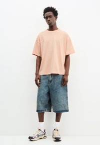 Lyserød oversized T-shirt, blå denim shorts til knæene og multicolore sneakers. Enkel design med korte ærmer og afslappet pasform.