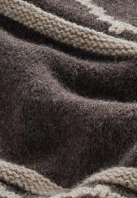 Mørkebrun uldstof med en fuzzy struktur, prydet med en lysere beige strib af strikkemønster langs kanten. Blød og varm udseende.