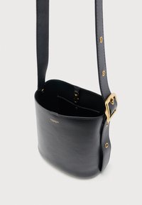 Μαύρη δερμάτινη τσάντα χιαστί με ρυθμιζόμενο ιμάντα, χρυσή αγκράφα και μικρή εσωτερική τσέπη, με διακριτικό χρυσό λογότυπο της μάρκας στο μπροστινό μέρος.