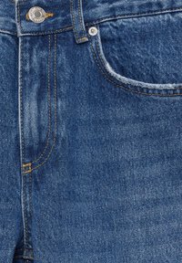 Jean en denim bleu en gros plan montrant la poche avant, le bouton en métal et les détails de couture jaune.