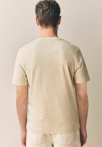 Beżowa koszulka z krótkim rękawem, wykonana z miękkiego materiału, z okrągłym dekoltem i subtelną teksturą. Prosty, elegancki design.