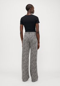 Black short-sleeve fitted top paired with high-waisted wide-leg pants featuring a gray and black wavy pattern. Smooth fabric texture.