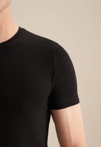 T-shirt noir en coton avec un col rond et des manches courtes. Présente une texture lisse et un design ajusté. Simple, sans motifs visibles.