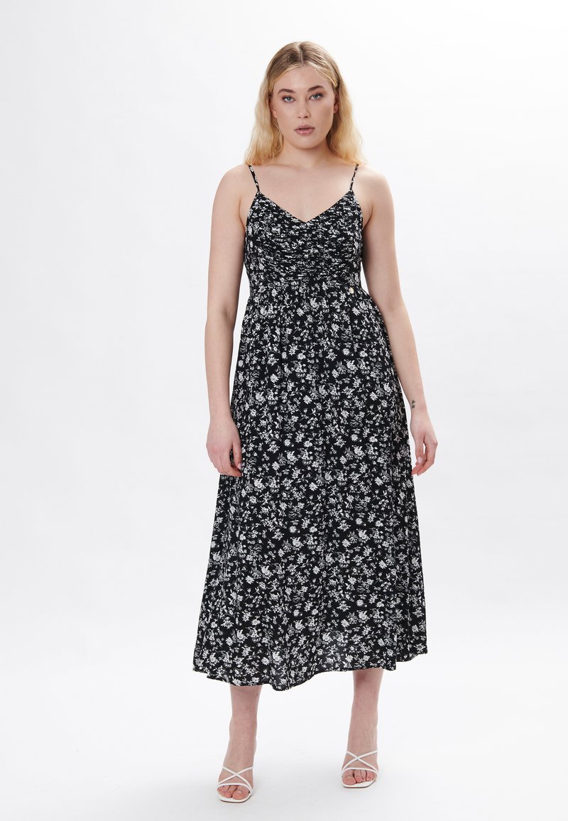 Schwarzes, blumiges Maxikleid mit dünnen Trägern, mit gerafft gearbeitetem Oberteil und fließendem Rock, verziert mit kleinen weißen Blüten.