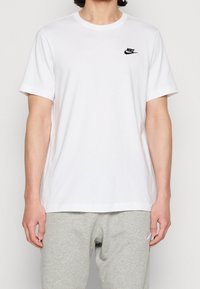 White Nike t-shirt, short sleeves, crew neckline, features small black logo on left chest, smooth cotton fabric, paired with light gray sweatpants.
