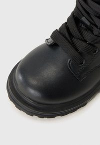 Musthave nahkasaapad, millel on ümar nina, tekstureeritud pind ja mustad nöörid. Saapad on varustatud kummist tallaga, millel on nähtav mustripattern.