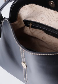 Borsa a tracolla nera in pelle con accessori dorati, interno beige con tasca con zip e foderatura a motivo logo color sabbia. Decorazioni cucite sui lati.