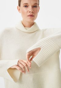 Pullover aus cremefarbenem Strick mit einem gerippten Kragen. Verfügt über weite Ärmel mit einem Ausschnittdesign und einem strukturierten Muster entlang des Körpers.