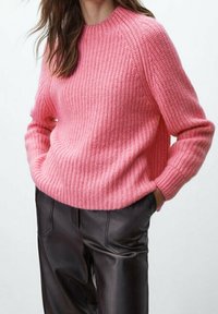 Maglione rosa lavorato a maglia con motivo a coste strutturato, collo rotondo e maniche raglan. Abbinato a pantaloni in pelle nera con tasche frontali.