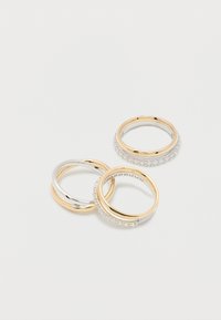 Τρεις διαπλεκόμενοι δακτύλιοι με χρυσές και ασημένιες λωρίδες, δύο διακοσμημένοι με μικρούς καθαρούς πολύτιμους λίθους, τοποθετημένοι πάνω σε λευκή επιφάνεια.