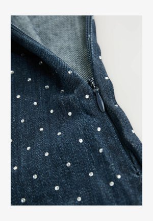 Tume sinine denimkangas, millel on hajutatud rhinestone'id ja nähtav tõmblukk äärtes, hele taust.