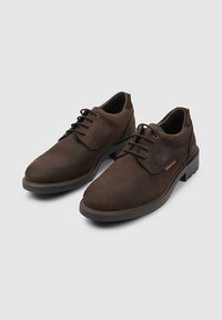 Zapatos de cuero marrón con una textura suave, punta redondeada y diseño de cordones. Presentan costuras sutiles y una suela de goma de perfil bajo.