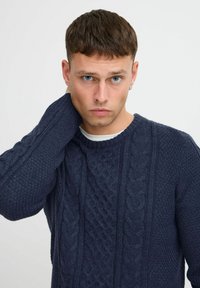 Pull en tricot bleu marine avec des motifs en mailles torsadées, un col ras du cou et des manches texturées. Fabriqué à partir d'un matériau en mélange de laine épais.