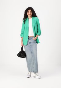 Zöld blézer, fehér crop top és világoskék farmer szoknya. Fekete mintás táska és fehér sportcipő teszi teljessé az öltözetet. Texturált anyagok.