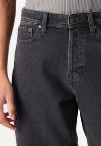 Svarta denimjeans har en klassisk femfickorsdesign, knäppning med knapp och subtila sömmar längs sömmarna.