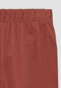 Legginsy w kolorze rdzy o miękkiej, gładkiej fakturze i elastycznym pasku w talii, z delikatnymi detalami szwów na górze.