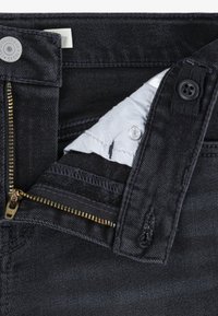 Σκούρο τζιν με brass φερμουάρ και μαύρο κουμπί. Διαθέτει γκρι επένδυση και ορατή ραφή, παρουσιάζοντας ένα κλασικό κόψιμο και φινίρισμα.