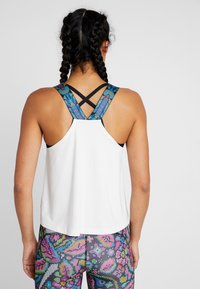 Wit sportief tanktop met een racerback ontwerp en blauwe en meerkleurige geometrische bandjes; gedragen met een legging met patroon.