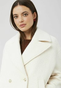 Manteau en mélange de laine blanche avec un design croisé, un col cranté et un tissu texturé. Comprend des boutons dorés brillants et une doublure douce.