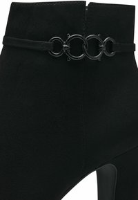 Sorte ankelstøvletter med en teksturert semsket finish som har en sirkulær metallkjedeaccent rundt ankelen og en høy hæl for heving.