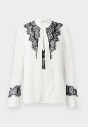 Weiße Bluse mit schwarzen Spitzenakzenten entlang des Kragens und der Ärmel, mit einer Schleife am Ausschnitt und Rüschensäumen.