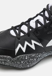 Chaussure de sport noire et blanche avec motif en zigzag, lacets noirs, languette en mesh blanche et semelle noire tachetée, vue de profil en gros plan.
