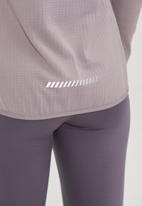 Lyse lilla, tekstureret træningstrøje med refleksstribe ved kanten, parret med mørkelilla, tætsiddende leggings.