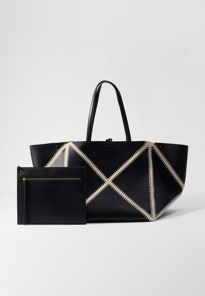 Black leather tote bag with cream stitching, featuring an angular design and two handles, accompanied by a matching black zip pouch.