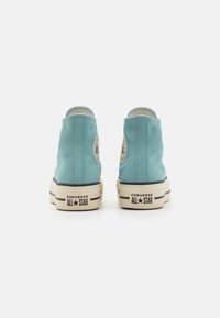 High-top sneakers in light blue suede with cream rubber soles. Features black stripes and round logo patch on each outer side.