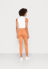Calças justas cor pêssego com cintura alta, pernas afuniladas e bolsos traseiros, combinadas com uma blusa sem mangas branca e ténis claros.