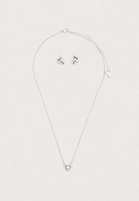 Σετ ασημένια κοσμήματα που περιλαμβάνει ένα λεπτό μενταγιόν σε σχήμα καρδιάς σε αλυσίδα και τα αντίστοιχα σκο υλαρίκια καρφάκια με αντανακλαστικές λεπτομέρειες.