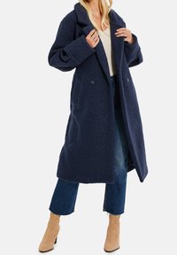 Marineblauer Wollmischmantel mit Doppelknöpfen, großen Revers und zwei Seitentaschen; zeichnet sich durch eine strukturierte Oberfläche und ein knielanges Design aus.