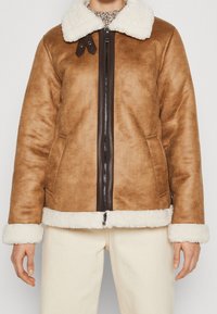 Brown faux shearling jacket with white fur collar and cuffs, zip closure, and dark brown accents at the neck and pockets.