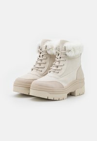 Botas beige con cordones y un collar de piel sintética, texturas de cuero liso y ante, suela gruesa de plataforma y detalles cosidos.