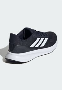 Black athletic shoe with a mesh upper, white stripes, and a cushioned white midsole. Features textured accents and a rounded toe design.