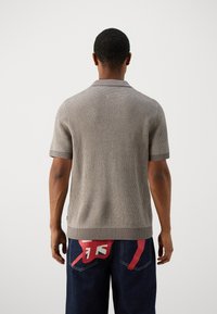 Krótki rękaw, teksturowane dzianinowe polo w jasnoszarym kolorze z ciemnoszarym kołnierzykiem. Noszone z ciemnoniebieskimi dżinsami z czerwonymi akcentami na kieszeniach.