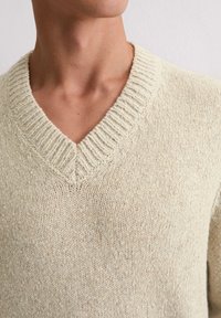 Hellesbeige V-Ausschnitt-Pullover mit strukturiertem Strickmuster. Rippkragen und dezente Flecken in Blau und Beige im gesamten Stoff.