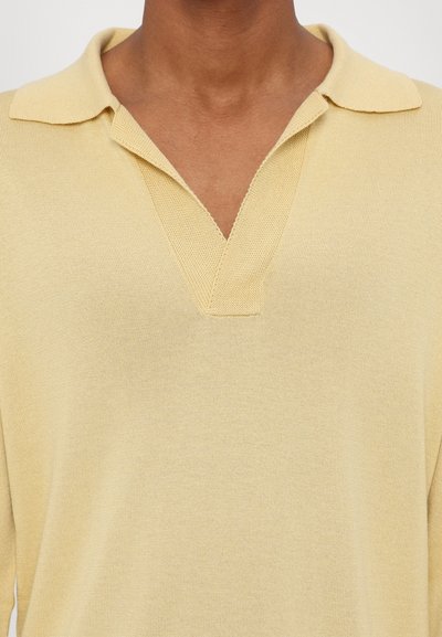 Gelbes Strick-Polohemd mit V-Ausschnitt, weichem Material und klassischem Kragen. Nahaufnahme zeigt die Nähdetails.