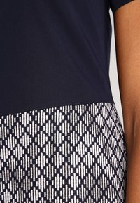 Zbliżenie na osobę w granatowej bluzce oraz czarno-białej spódnicy lub spodniach w geometryczny wzór.