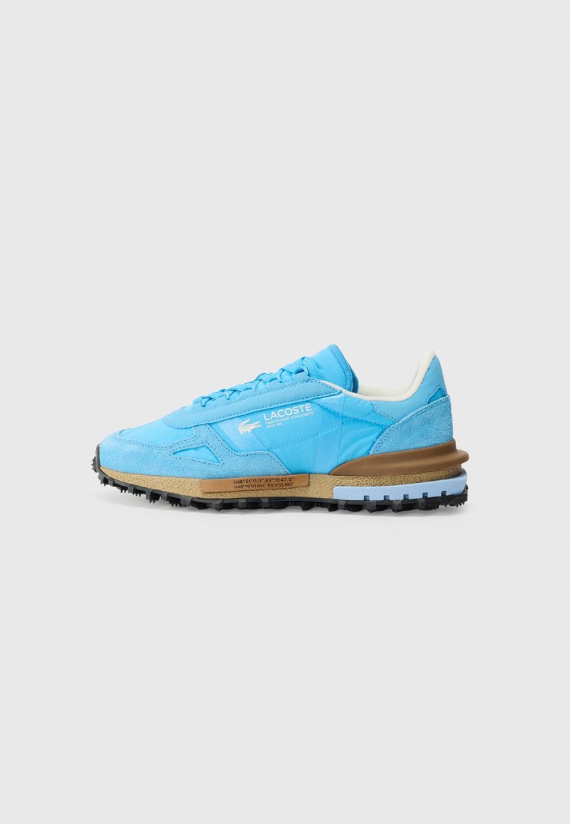 Baskets Lacoste bleu clair avec des accents en daim, une doublure intérieure blanche et une semelle noire robuste sur une semelle intermédiaire beige sur fond gris clair.