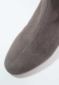 Gros plan sur l'avant d'une chaussure en daim gris avec une couture centrale double sur un fond blanc uni.