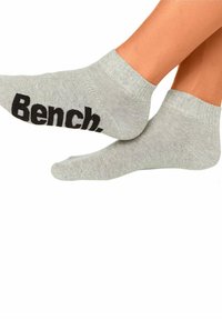 Harmaat nilkkasukat, joissa on ribbireunat, ja joissa on suuri musta "Bench."-logo. Kangas näyttää sileältä ja siinä on hieman joustava rakenne.