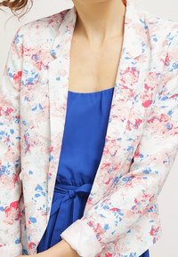Floral blazer featuring a white background with pink and blue patterns, structured shape, and long sleeves with light cuffs.